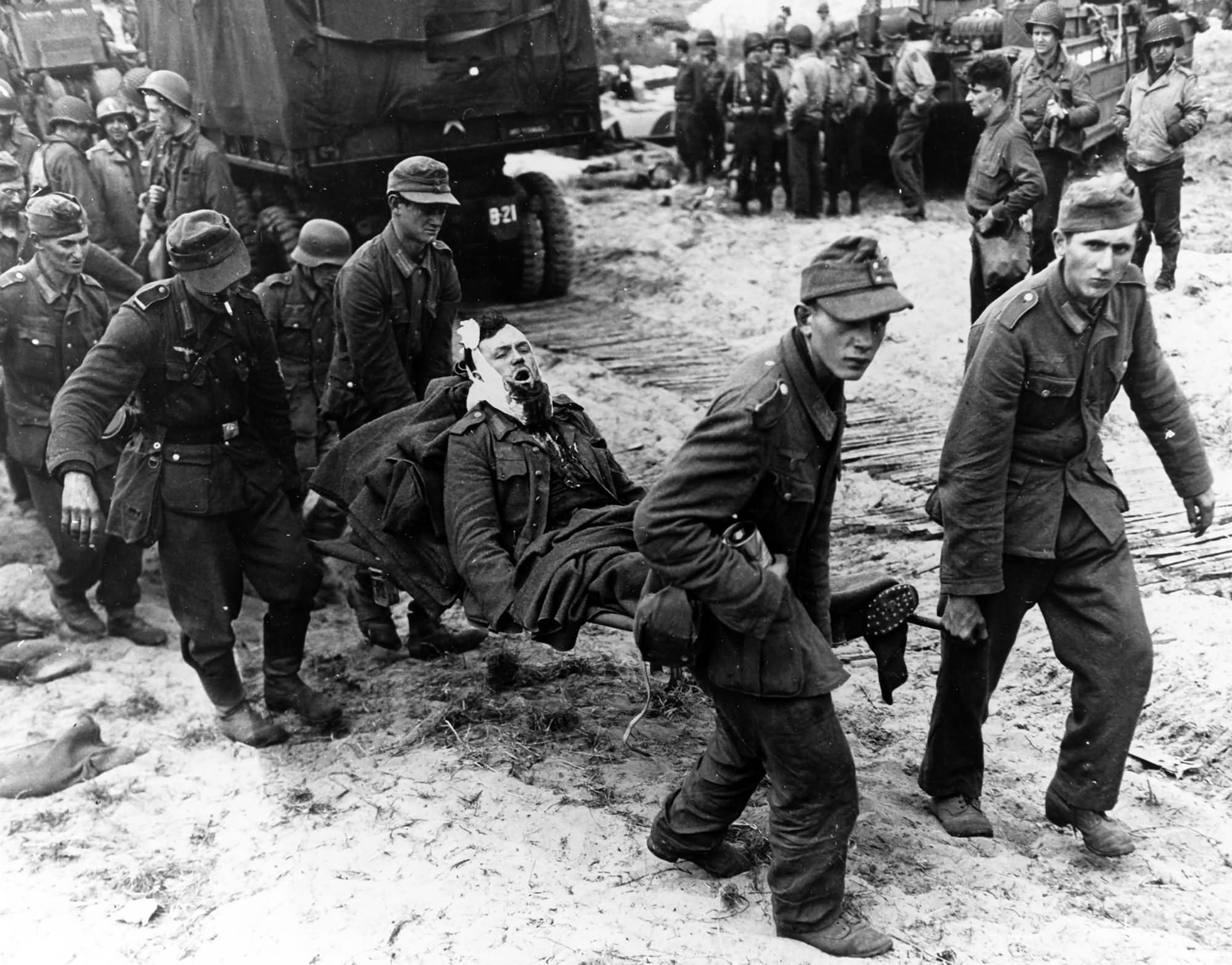 German POW carry wounded comrades to landing craft on a Normandy beach
