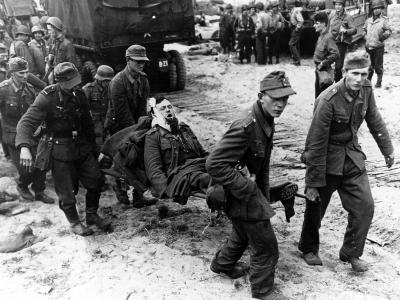 German POW carry wounded comrades to landing craft on a Normandy beach