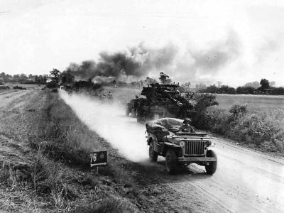 Troops pass burning German equipment on road to combat zone Falaise, Summer 1944