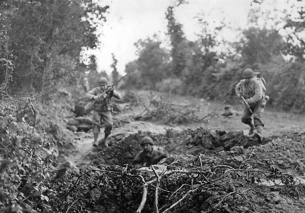US Infantrymen leap for safety of shell hole in Normandy