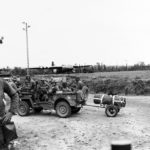 Infantrymen in Jeep get directions from a MP at a Normandy crossroads