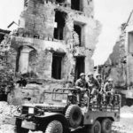 Troops and Dodge WC63 truck amid ruins of Trevieres 1944