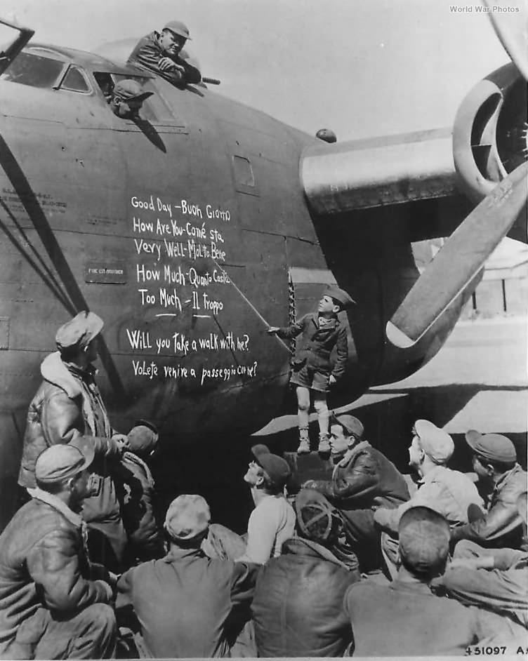 Small boy uses the side of a B-24 as a blackboard to give US airmen a lesson in Italian 44