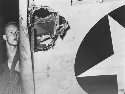 Crewman inspects Japanese 20mm cannon shell hole in F4F August 1942