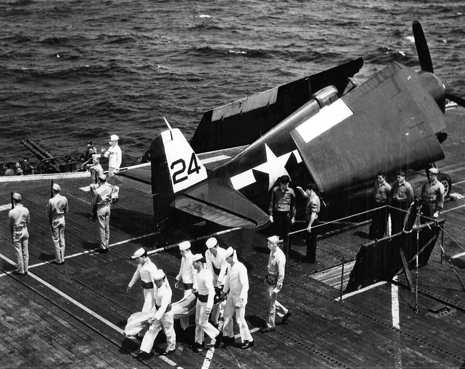 An Honor Guard carries the flag draped body of a shipmate from the deck elevator in preparation for a burial at sea on board the carrier Bataan CVL-29 1945