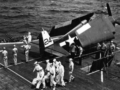 An Honor Guard carries the flag draped body of a shipmate from the deck elevator in preparation for a burial at sea on board the carrier Bataan CVL-29 1945