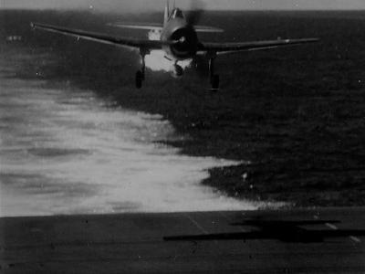 Grumman F6F-3 Hellcat flown by Lieutenant (jg) A. Magee of VF-25 streams flame as it approaches the carrier USS Cowpens CVL-25 – November 20, 1943