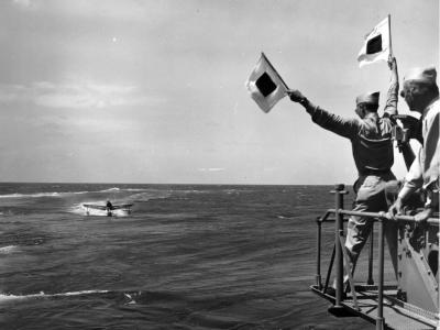 Personnel signal an approaching OS2U from an unidentified ship