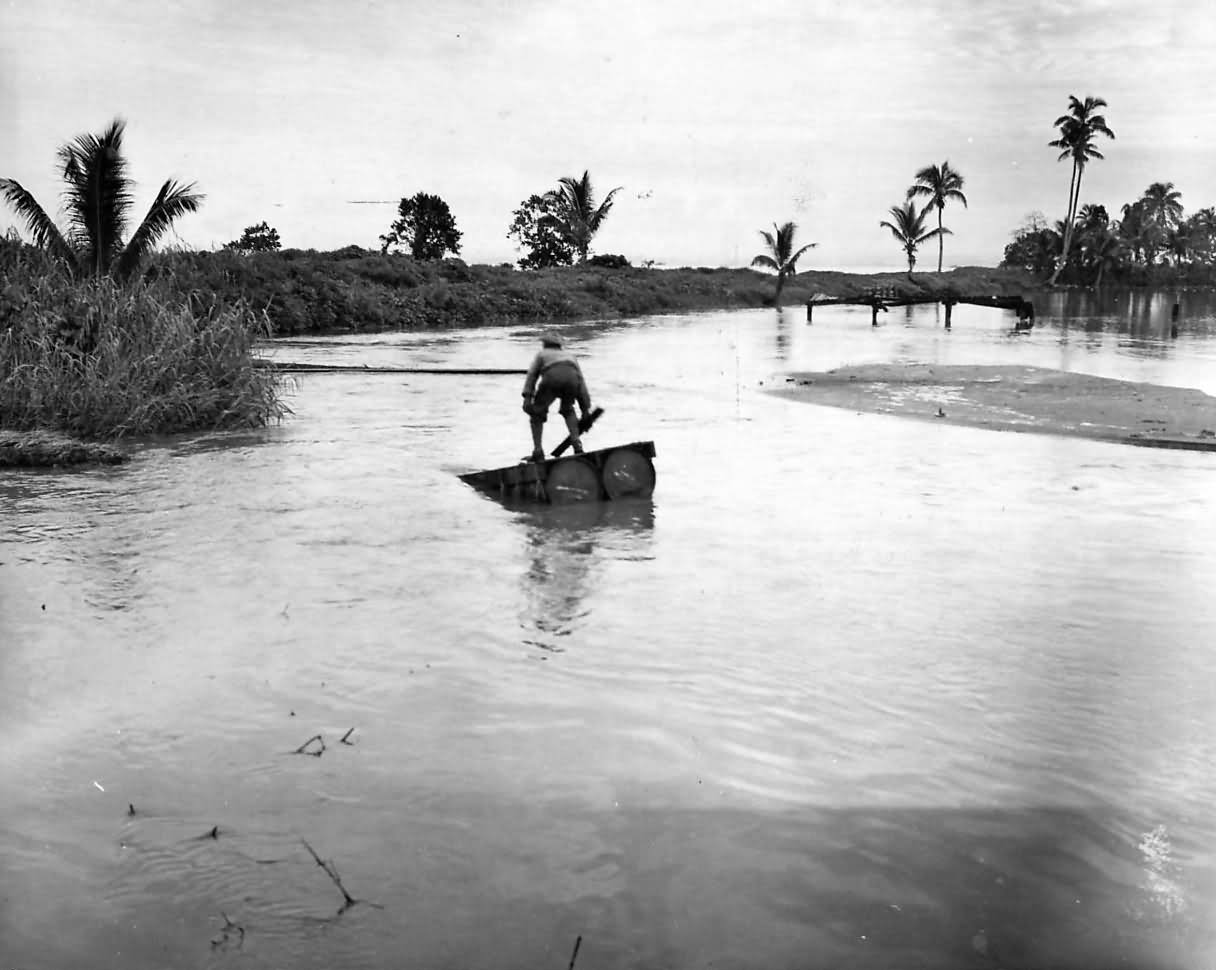 Marine uses a raft to cross a flooded road during the rainy season on Guadalcanal