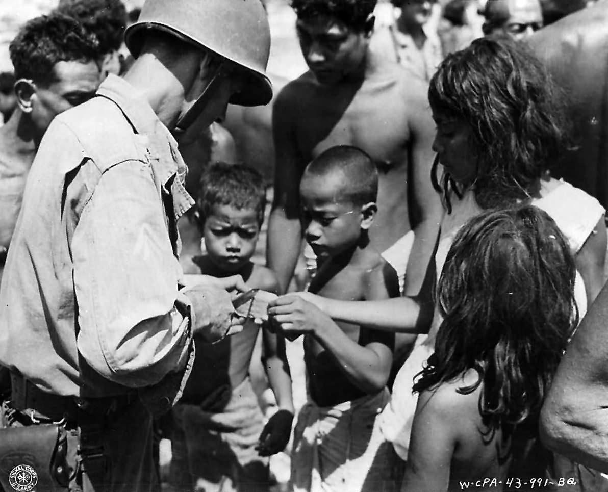 US officer of the 165th Infantry cuts up a piece of canned meat for hungry children