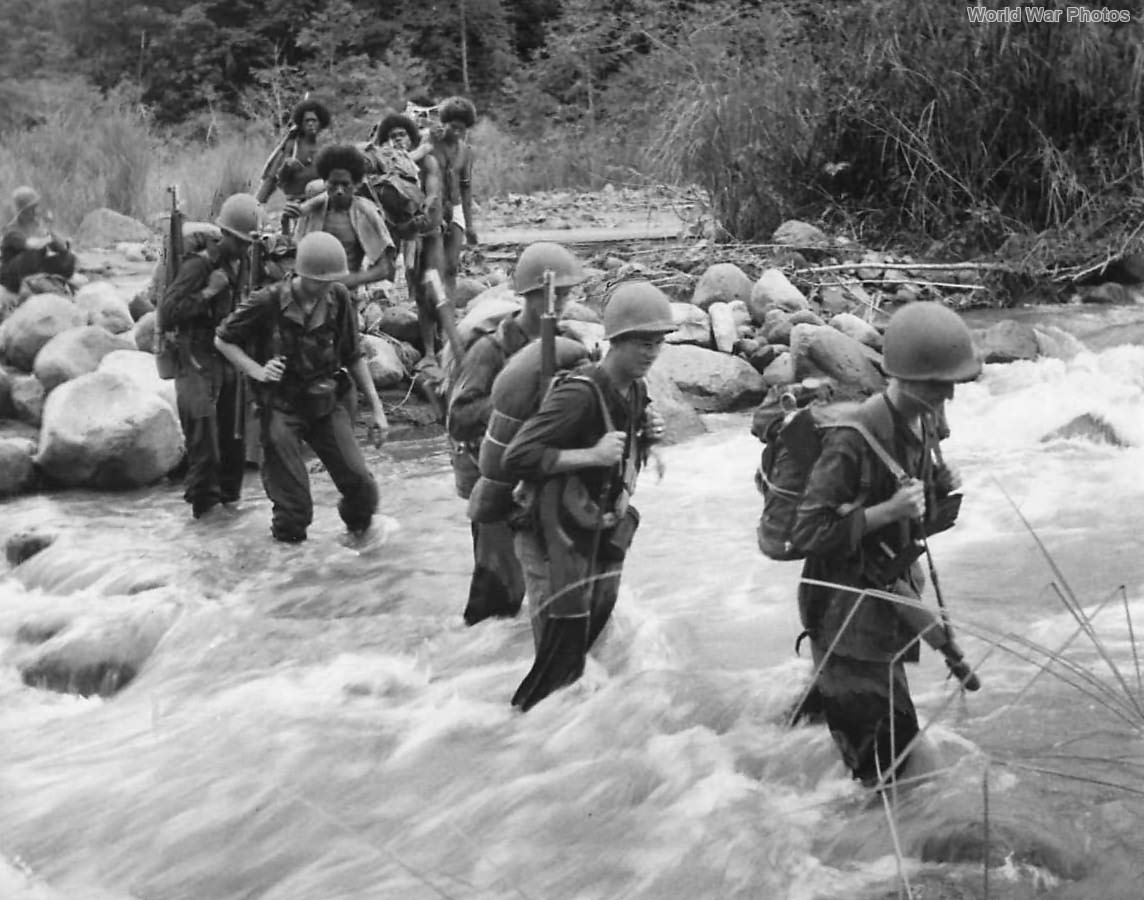 US troops and native porters cross stream in New Guinea 1942