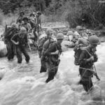 US troops and native porters cross stream in New Guinea 1942