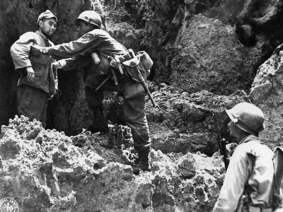 US 10th Army rifleman with the 32nd Infantry 7th Division searches a Japanese prisoner who has just emerged from a cave on Okinawa