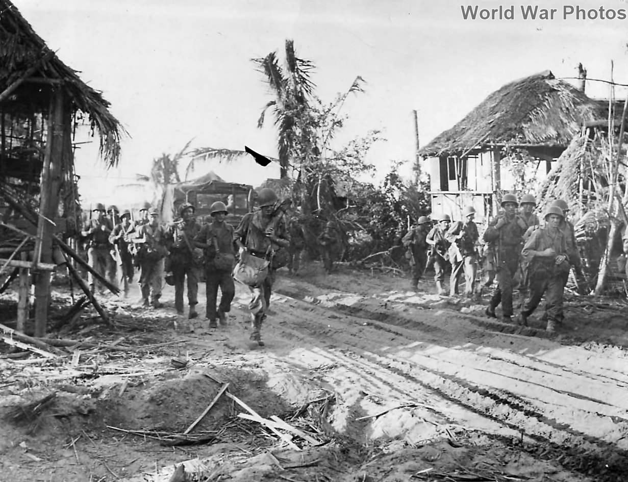 Troops move thru ruins of native village on Luzon 1945
