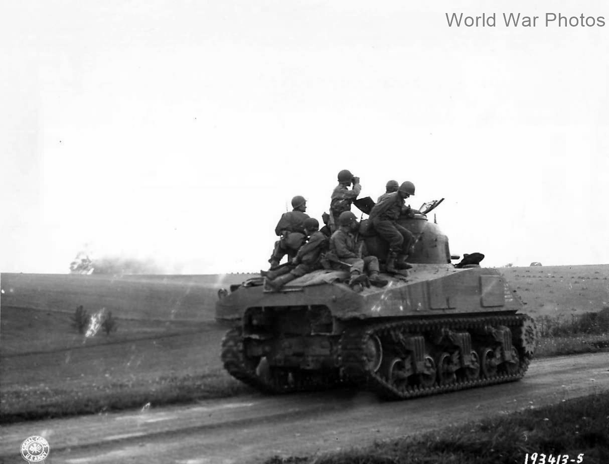 Troops on M4 tank watch artillery blast German position France 1944