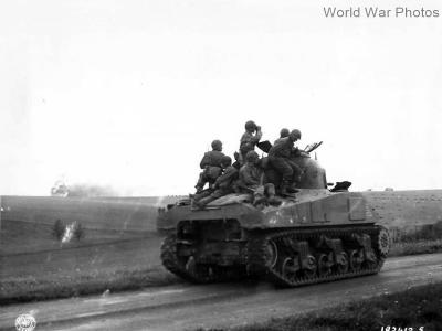 Troops on M4 tank watch artillery blast German position France 1944