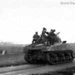 Troops on M4 tank watch artillery blast German position France 1944